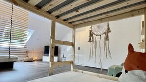 A modern bedroom with a wooden ceiling, a large bed, a dreamcatcher, and a view of the outdoors.
