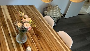 A wooden dining table with a vase of flowers, candles, and a hanging light fixture.