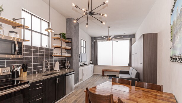 Een moderne keuken met een eethoek, met een houten tafel, zwarte kastjes en een groot raam.
