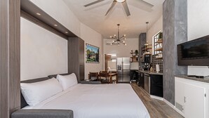 Een moderne hotelkamer met een groot bed, een bureau, een kitchenette en een televisie.