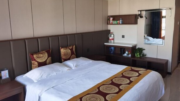A hotel room with a large bed, a bedside table, a mirror, a shelf with toiletries, and a window with curtains. - Erenhot Hualian International Hotel (Erenhot)