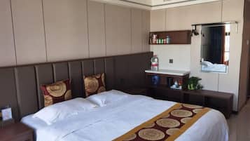 A hotel room with a large bed, a bedside table, a mirror, a shelf with toiletries, and a window with curtains.