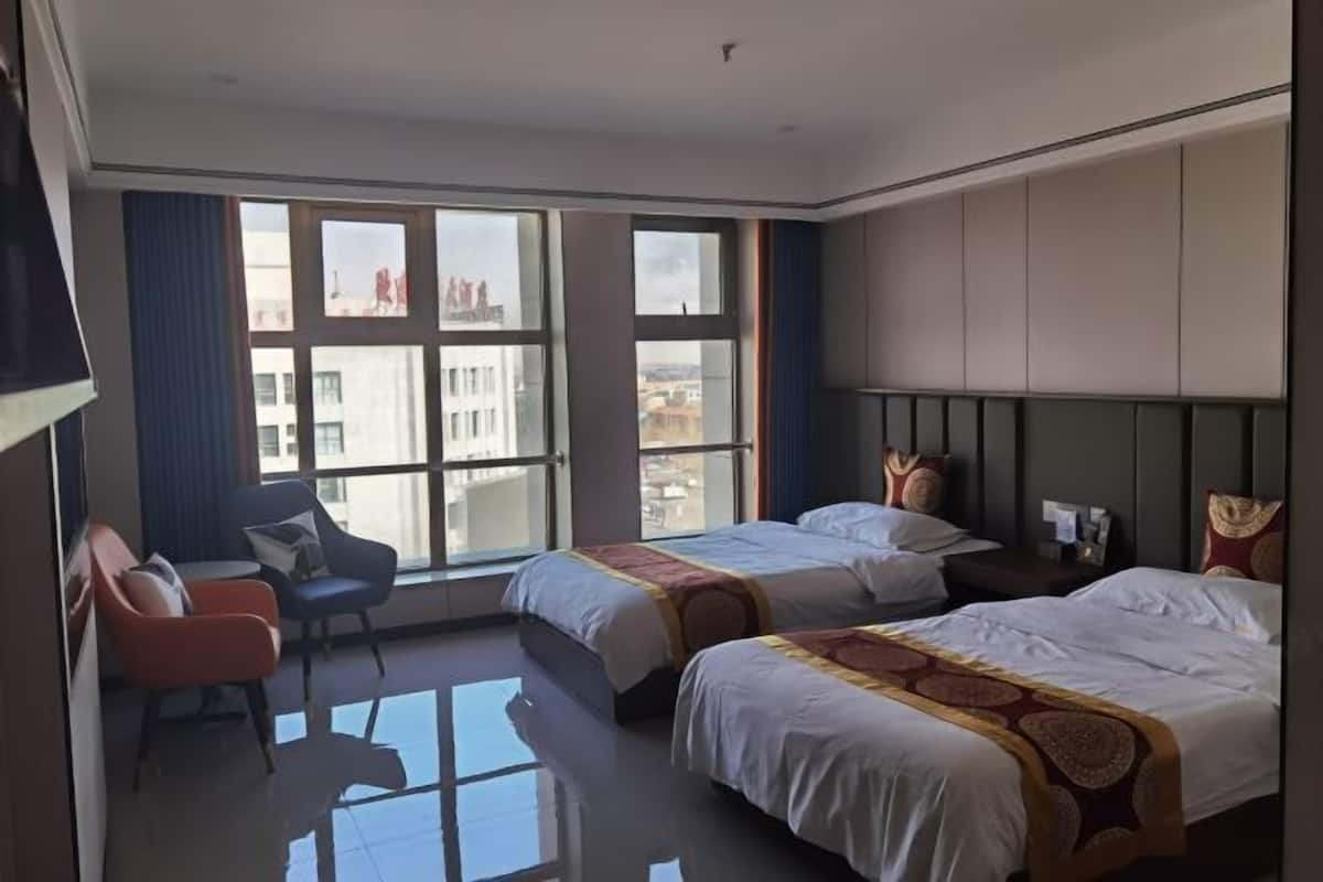 A hotel room with two beds, a sofa, and large windows.