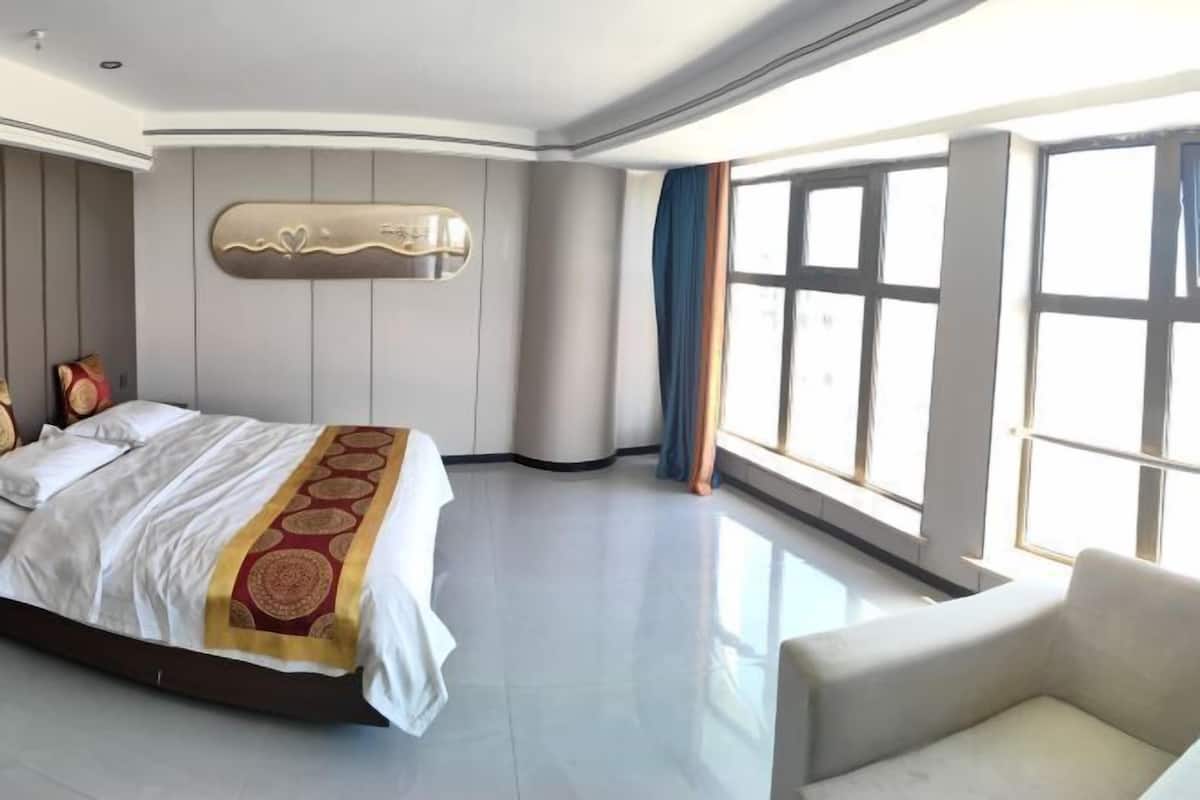 A modern hotel room with a large bed, a sofa, and a large window providing a view.