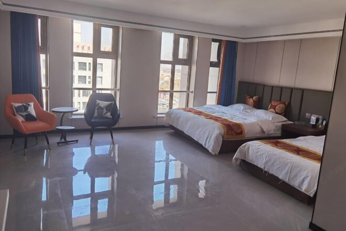 A hotel room with a large bed, a smaller bed, a chair, a table, and large windows.
