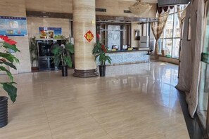 Un vestíbulo amplio con mostrador de recepción, plantas en macetas y un gran pilar con un emblema decorativo.