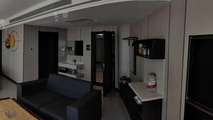 Una sala de estar moderna con un sofá, una mesa de centro, un televisor y una zona de cocina con un lavamanos y armarios.