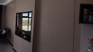 Una habitación de hotel con ventana, una silla, un estante con objetos y una botella de agua.