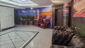 A lobby with a marble floor, a leather sofa, a mural of a sunset, and a reception area with chairs. - Erenhot Hualian International Hotel (Erenhot)