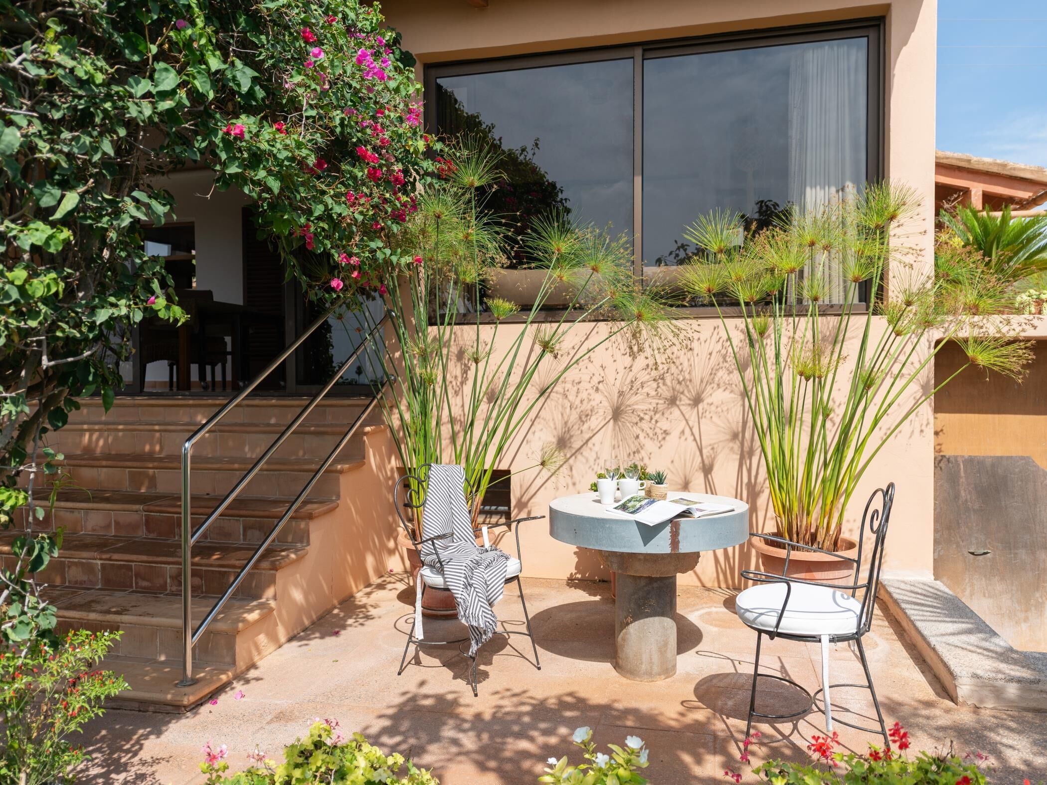A patio with a round table, two chairs, and potted plants.