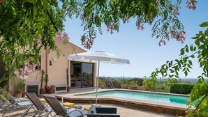 A poolside area with lounge chairs, a covered seating area, and a view of the landscape.