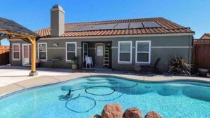 A residential property with a swimming pool, a covered patio, and a fenced backyard.