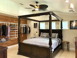A four-poster bed with a wooden headboard, a ceiling fan, and a wall-mounted shoe rack with clothes.