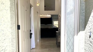 A hallway leading to a room with a television, a door, and a welcome mat.