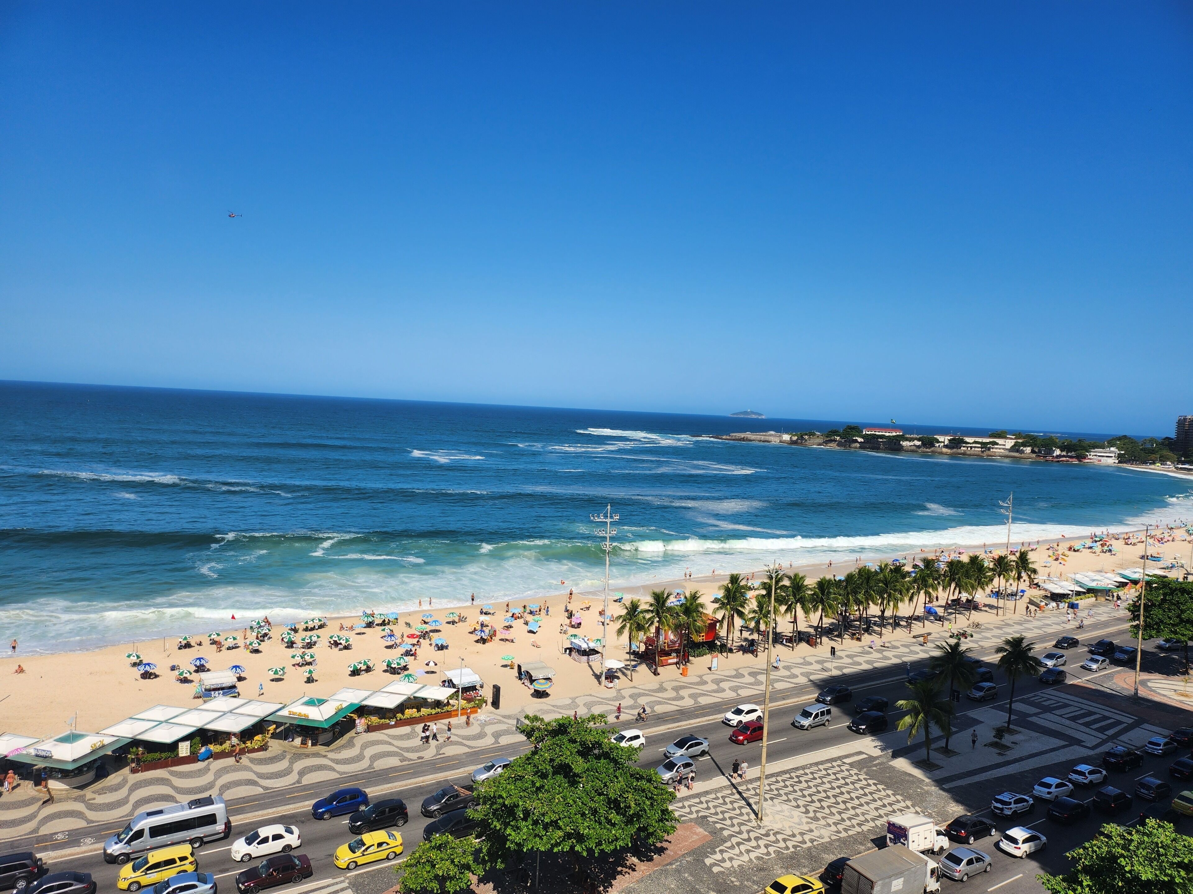 A beachside view with a road, parked cars, and beach umbrellas.