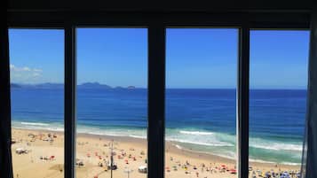 Vista de la playa a través de una ventana, con cielo despejado, mar tranquilo y gente disfrutando en la playa.