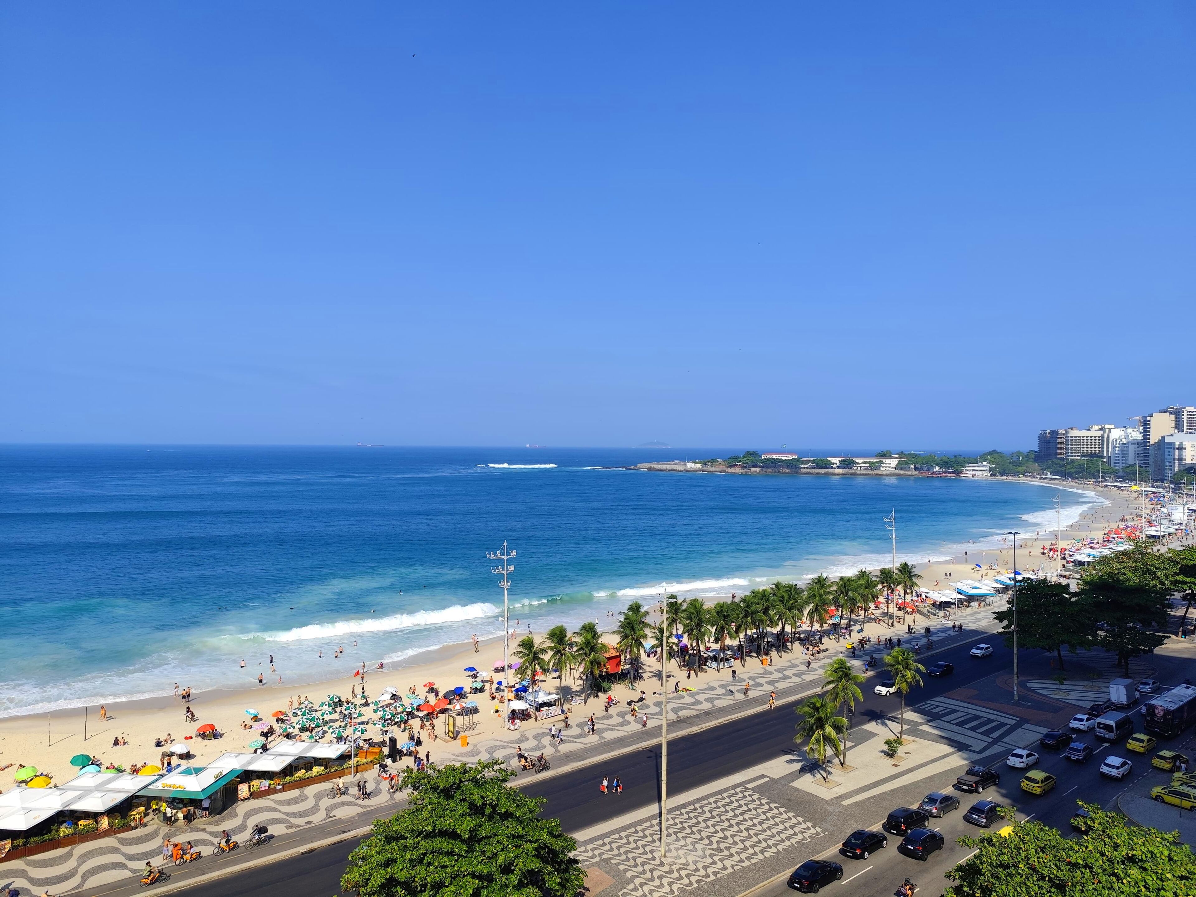 A coastal cityscape with a beach, palm trees, and a busy street.