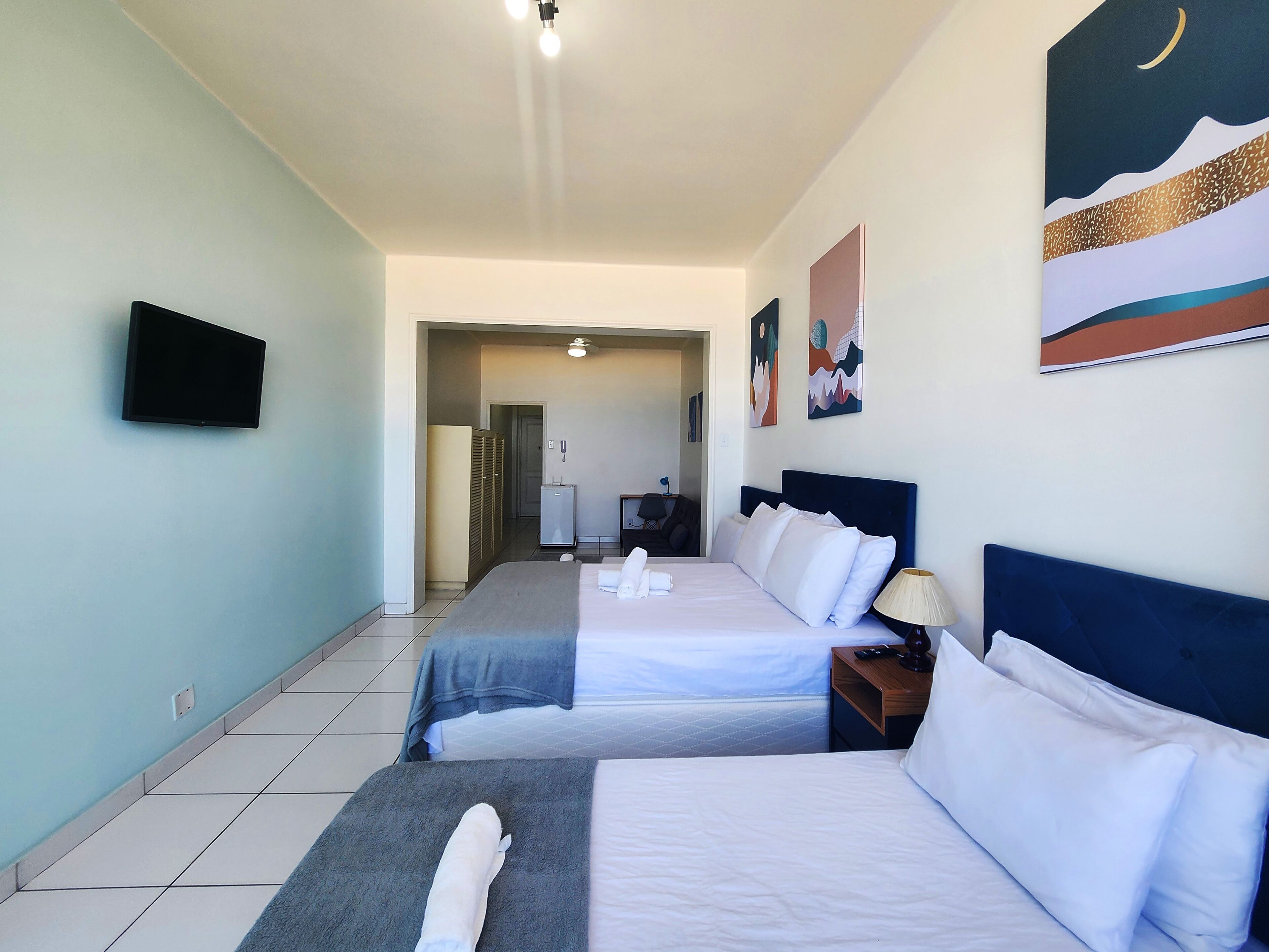 Ein Hotelzimmer mit zwei Betten, einem Fernseher, Bildern an den Wänden und Blick aufs Meer.