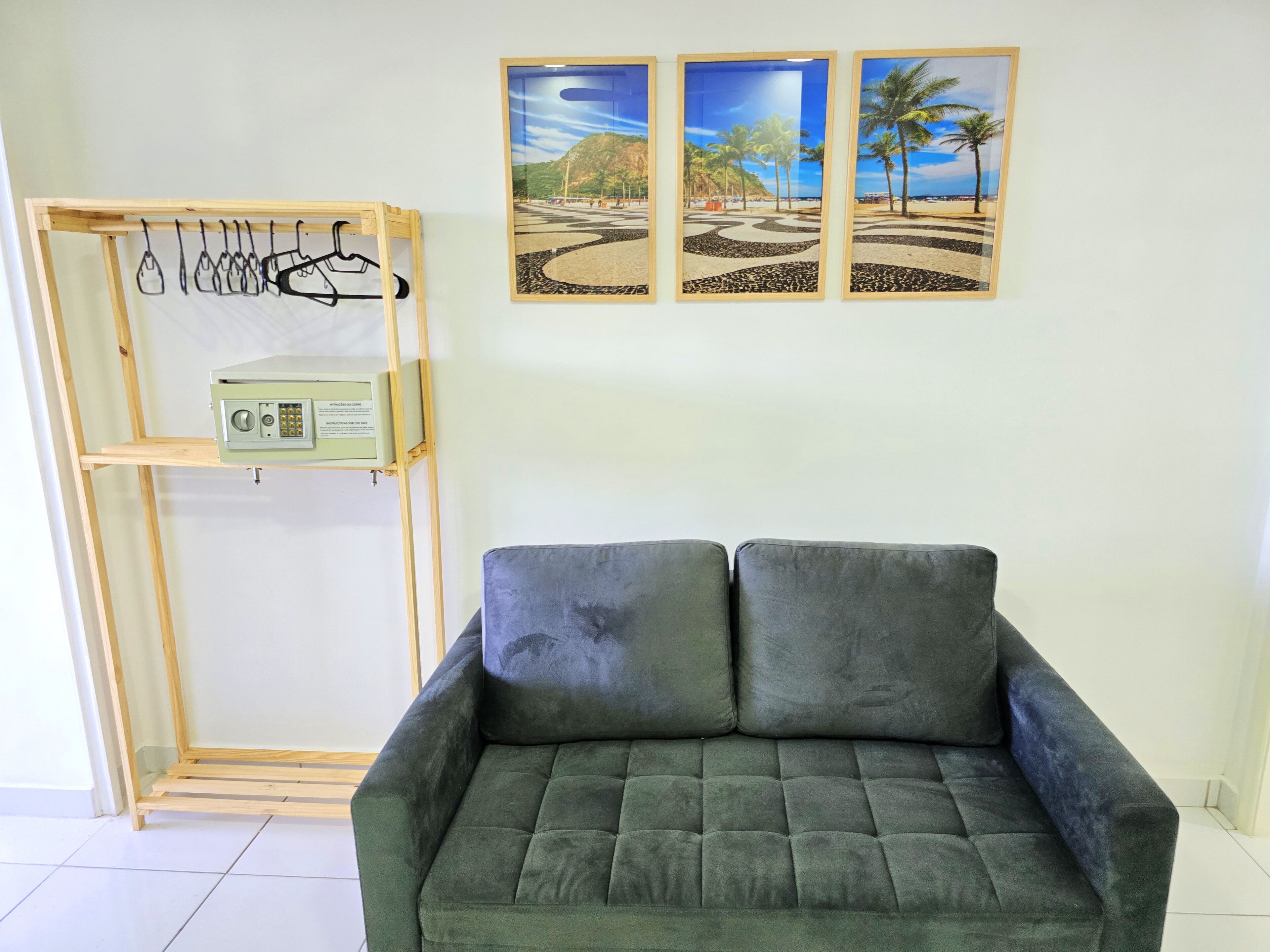 Une pièce avec un canapé gris, un étendoir en bois sur lequel sont suspendus des vêtements, et trois photos encadrées représentant des plages, accrochées au mur.