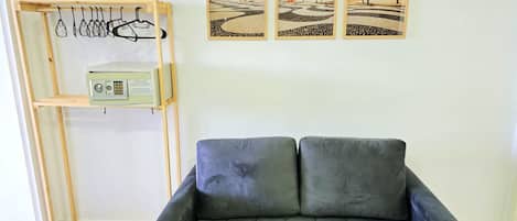 A room with a grey sofa, a wooden drying rack with clothes, and three framed beach pictures on the wall.
