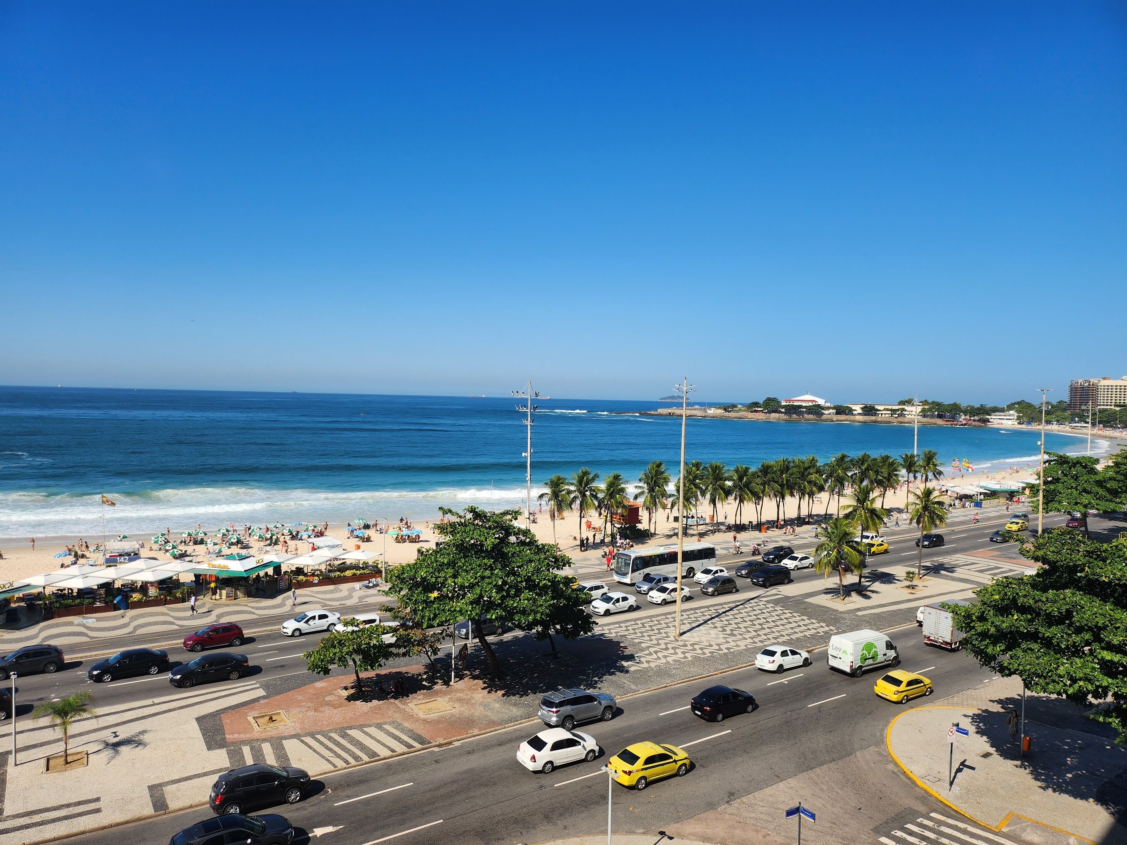 A coastal cityscape with a beach, palm trees, and a busy street with cars and taxis.