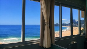 A room with large windows overlooking a beach, a curtain, and a vent. - Ocean View Copacabana Best Spot (Rio de Janeiro)