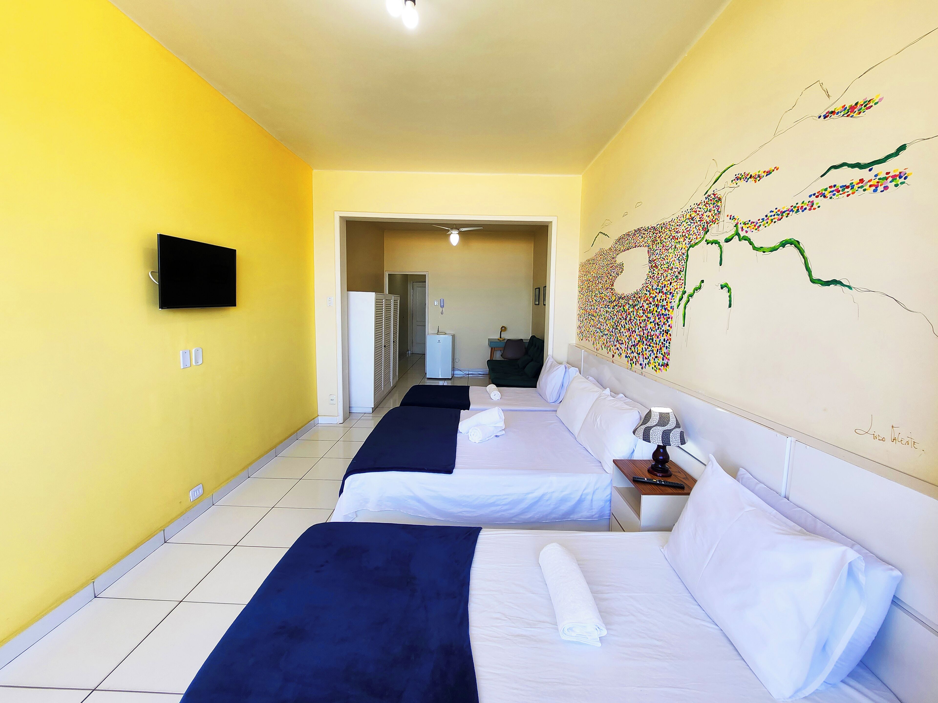 Camera d'albergo con due letti, una TV a schermo piatto, una mappa appesa al muro e una ventola a soffitto.