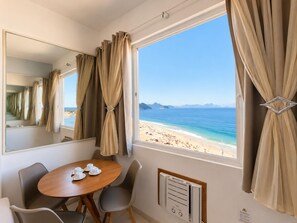 A room with a large window, a dining table with chairs, a mirror, and a wall-mounted air conditioning unit. - Ocean View Copacabana Best Spot (Rio de Janeiro)