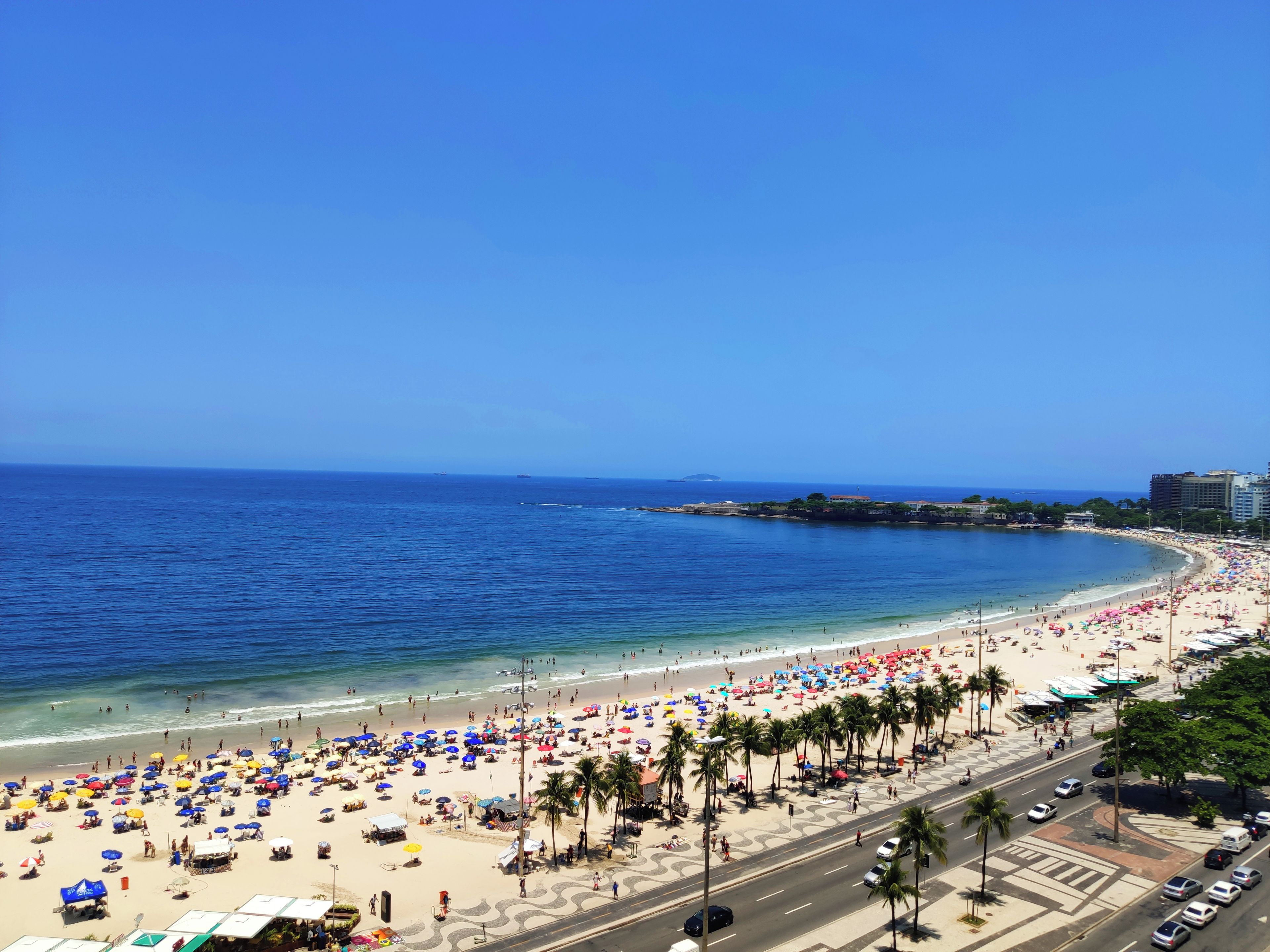 Una spiaggia con una strada che costeggia la riva, palme e cielo azzurro limpido.