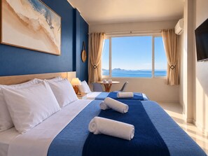 A hotel room with a large bed, two smaller beds, a desk, a chair, a TV, and a window with a view of the sea. - Ocean View Copacabana Best Spot (Rio de Janeiro)