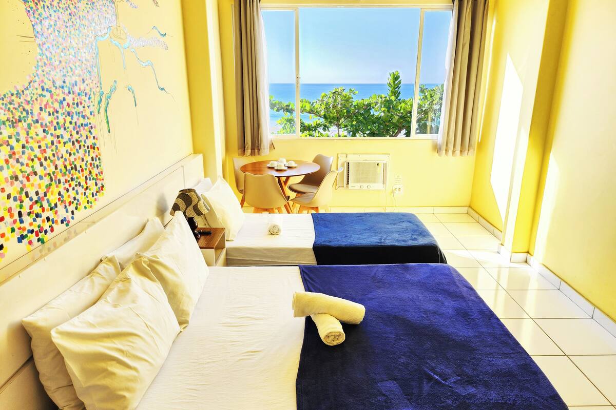 A hotel room with two beds, a dining area, and a view of the sea.