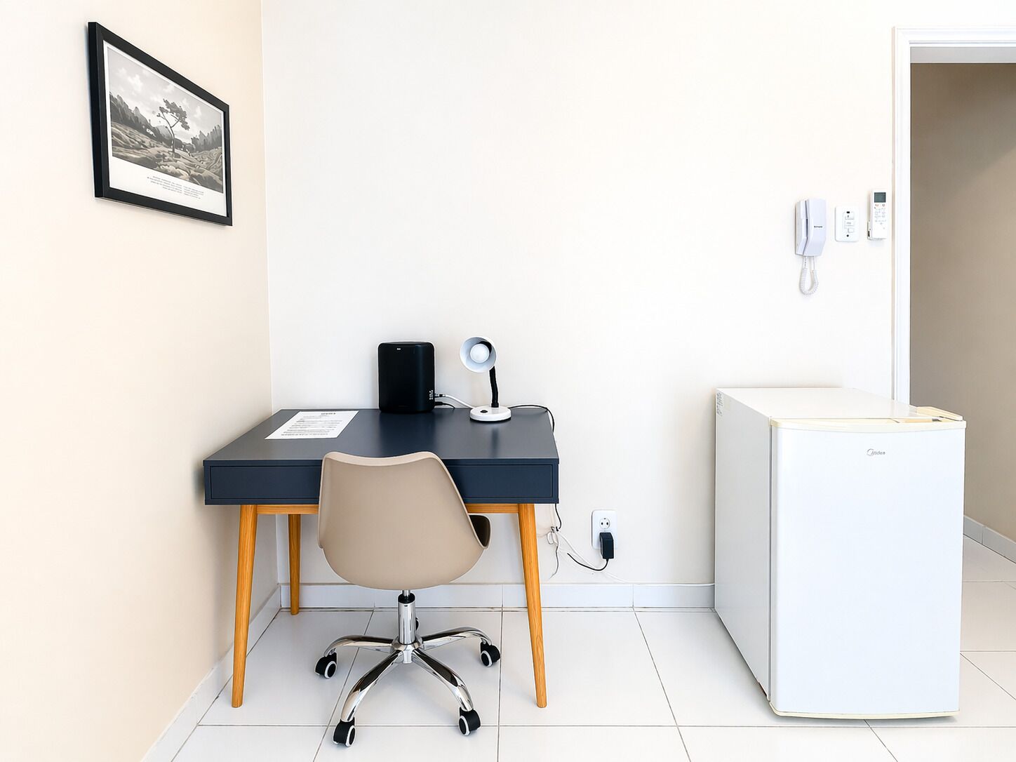A small office with a desk, chair, and a white refrigerator.