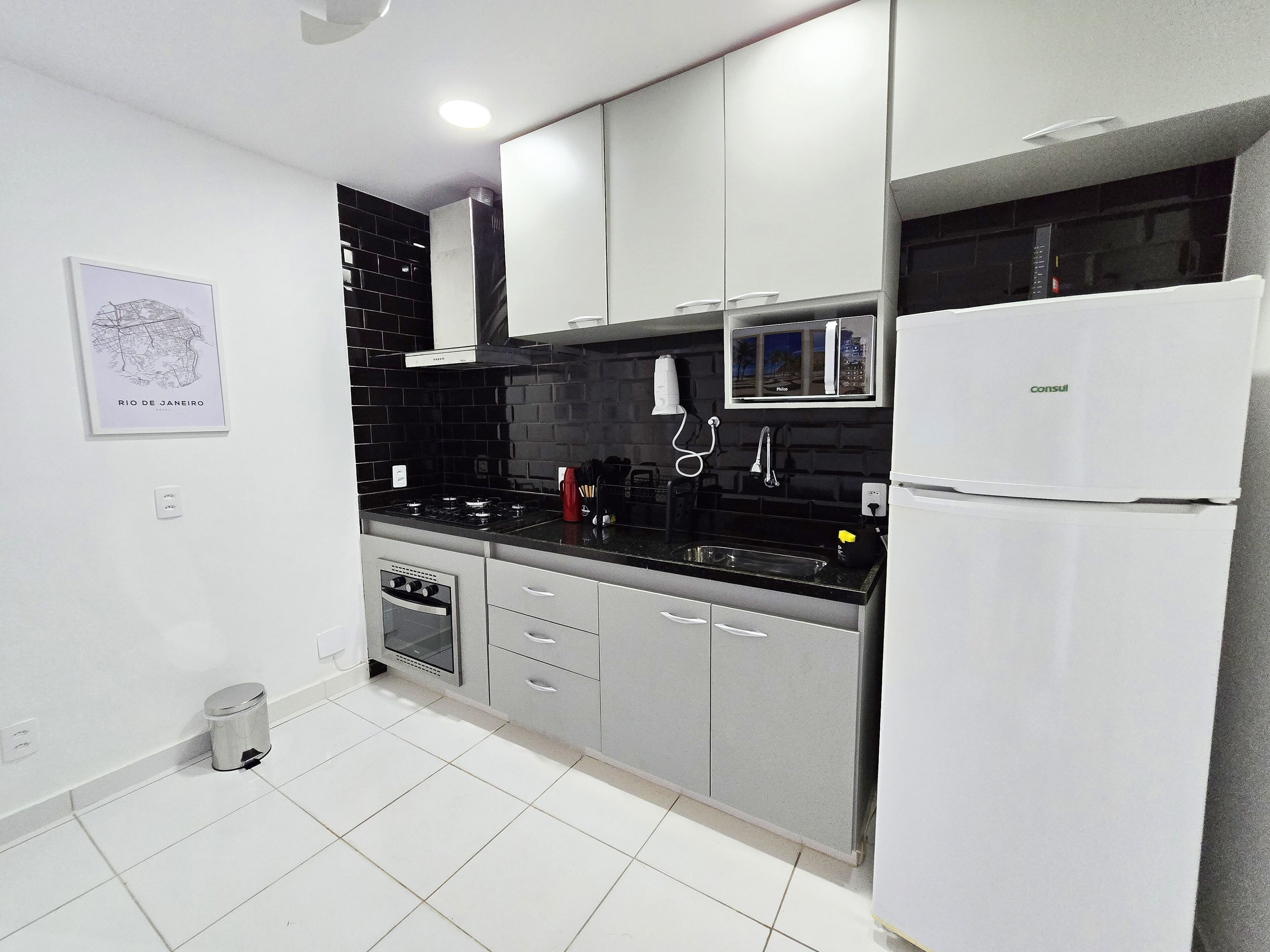 A modern kitchen with grey cabinets, a black countertop, a microwave, a refrigerator, and a sink.