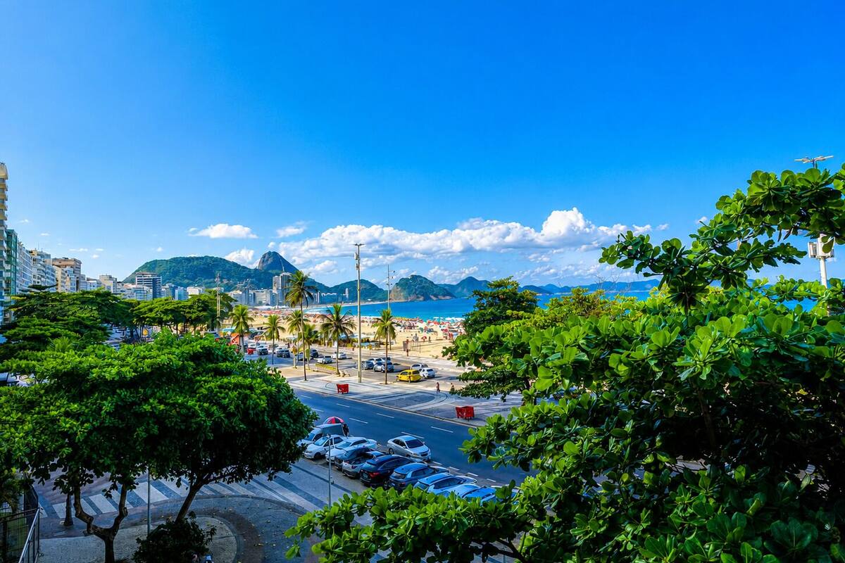 A coastal cityscape with a beach, palm trees, and a clear blue sky.