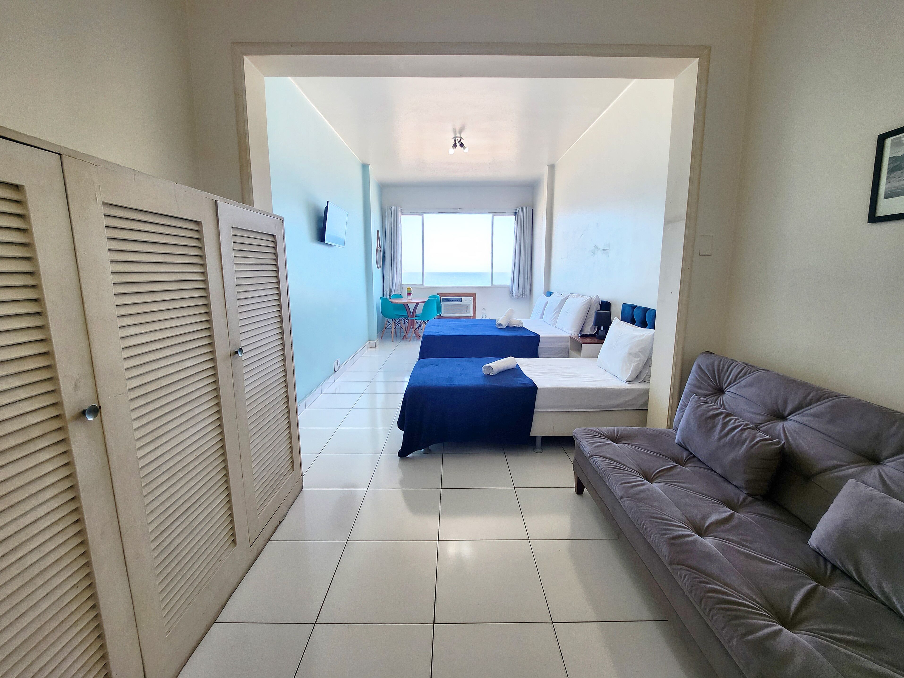 A hotel room with two beds, a sofa, a TV, and a dining area with chairs and a table.