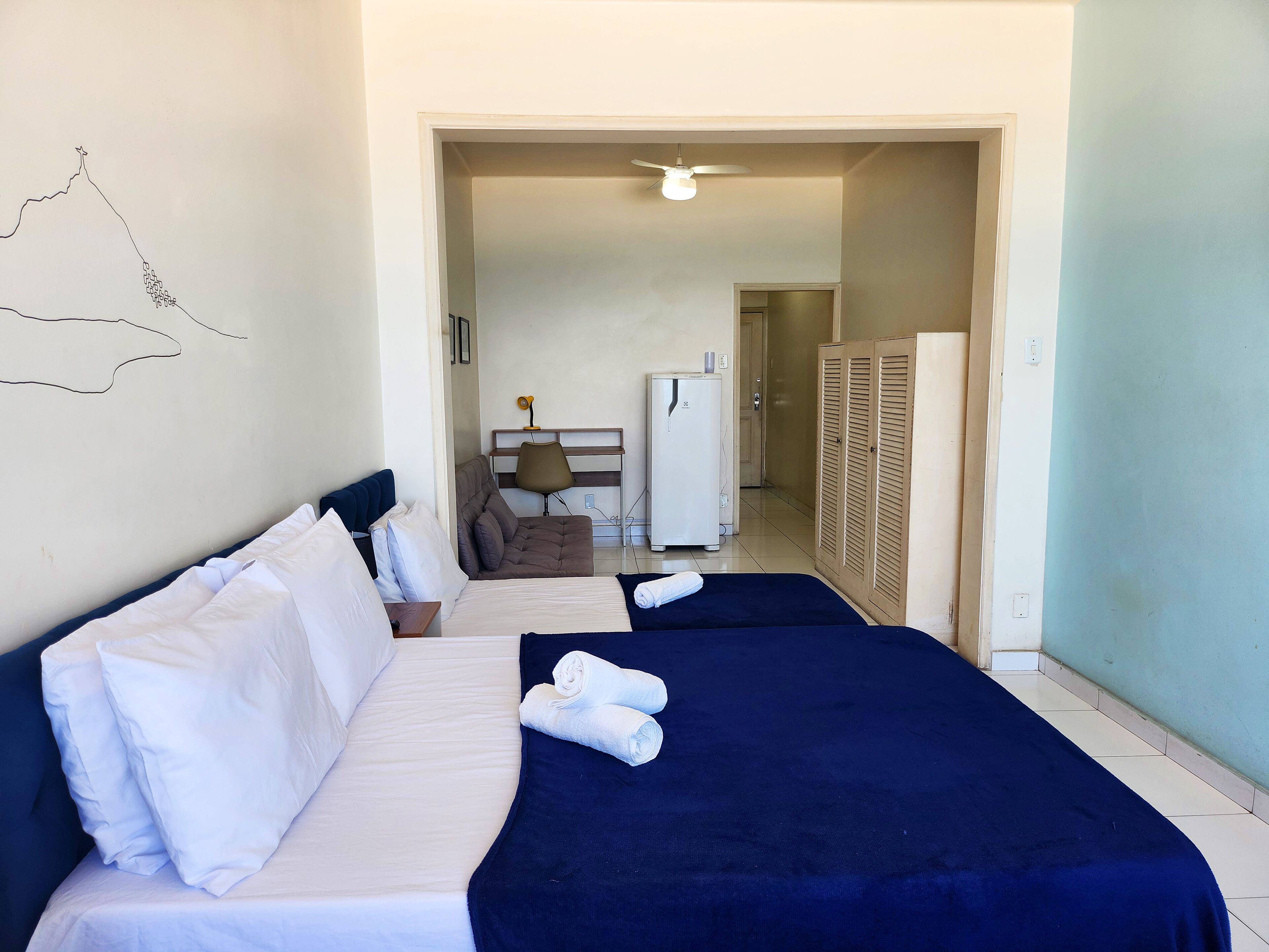 Een hotelkamer met twee bedden, een bureau met stoel, een koelkast en een kledingkast.
