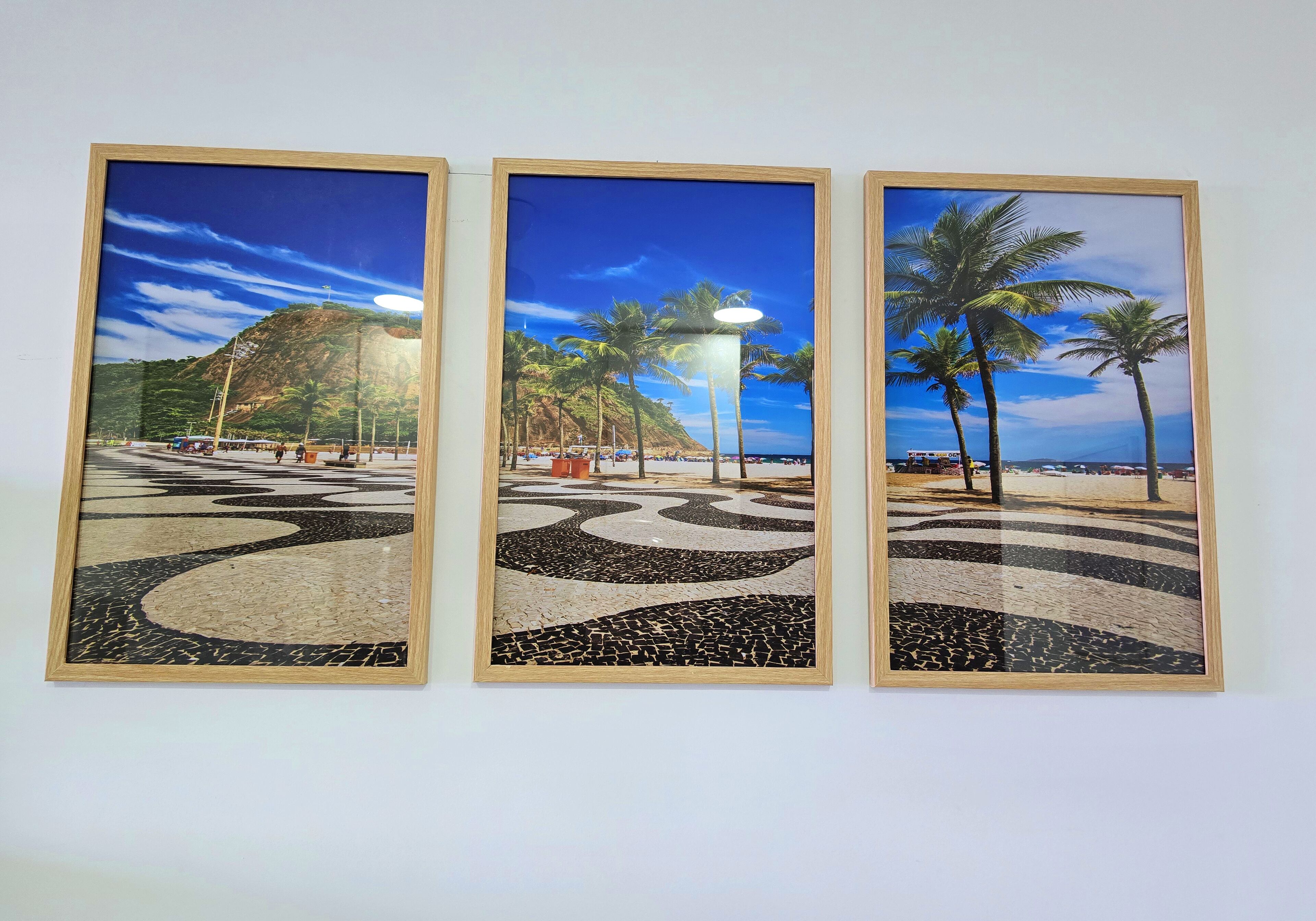 Three framed photographs of a beach scene with palm trees, a street lamp, and a mountainous background.