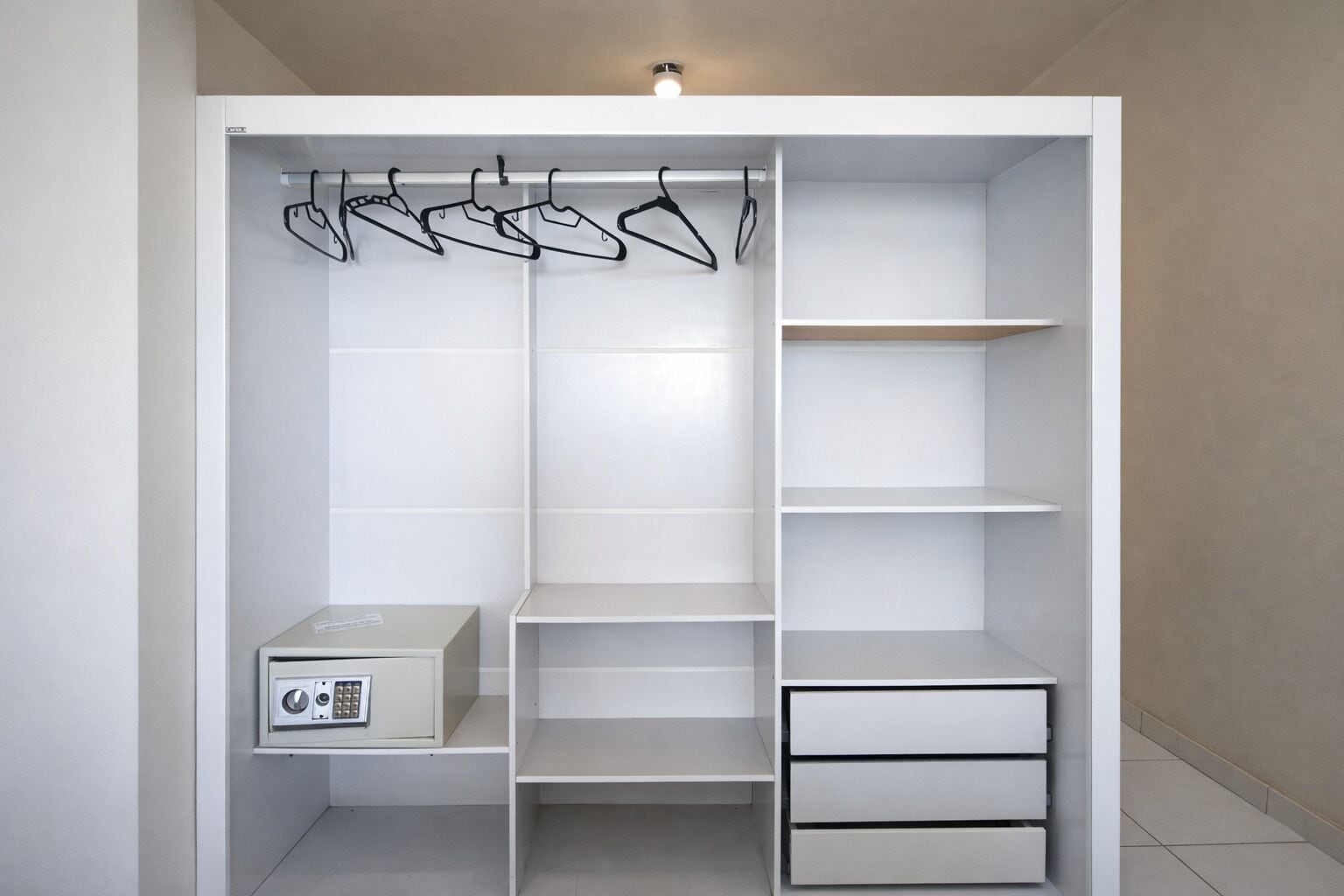 Un armario blanco con varias repisas, una barra para colgar ropa y un mueble para electrodomésticos.