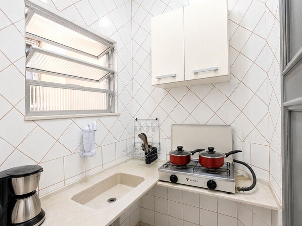 A kitchen with a gas stove, a coffee maker, and a window with blinds.