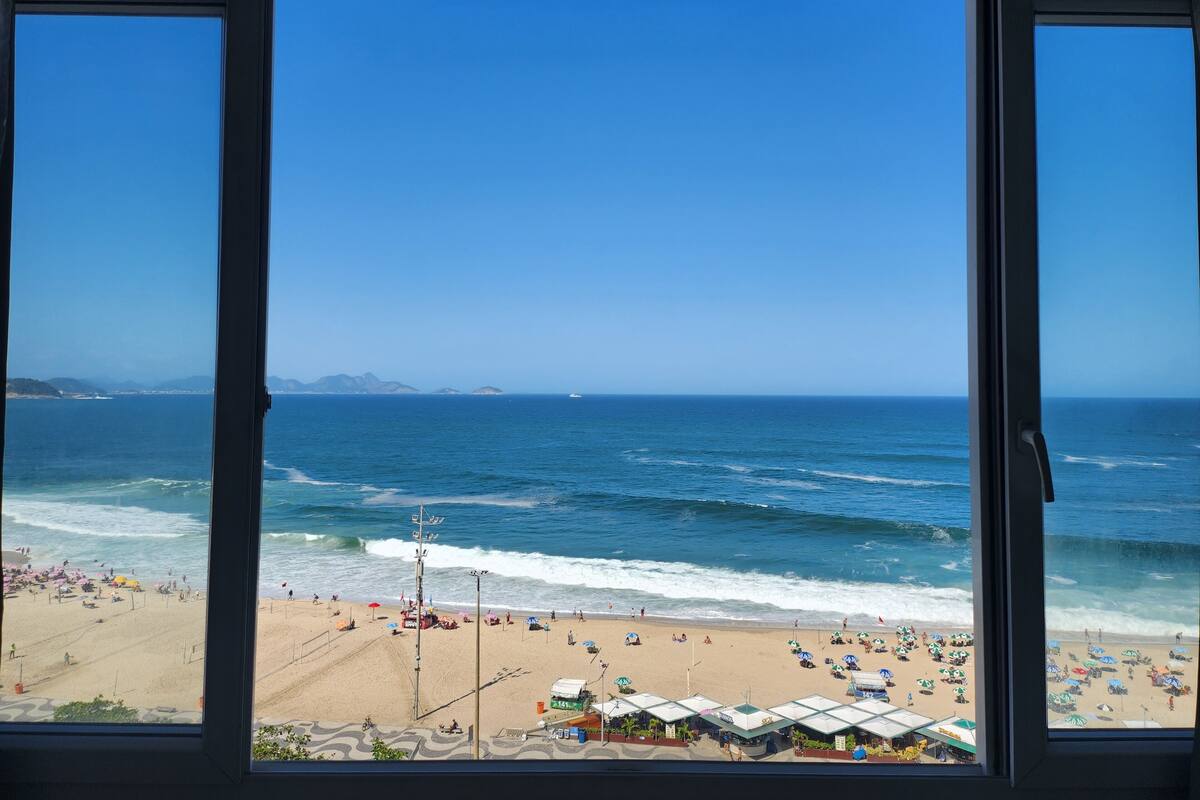 A beach view through a window, including the ocean, beach, and distant mountains.