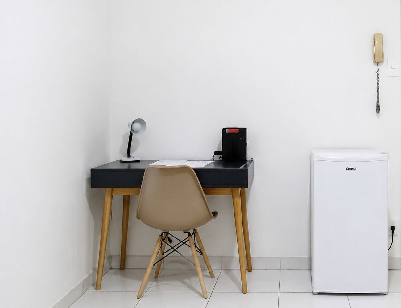 A small office space with a desk, chair, and a white refrigerator.