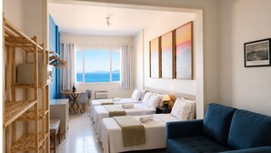 A hotel room with a bed, a desk, a chair, a blue sofa, and a view of the sea. - Ocean View Copacabana Best Spot (Rio de Janeiro)