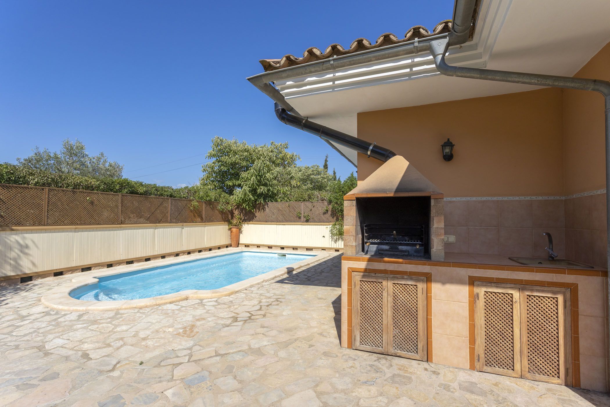 Un jardin avec une piscine, un espace barbecue et une terrasse en pierre.