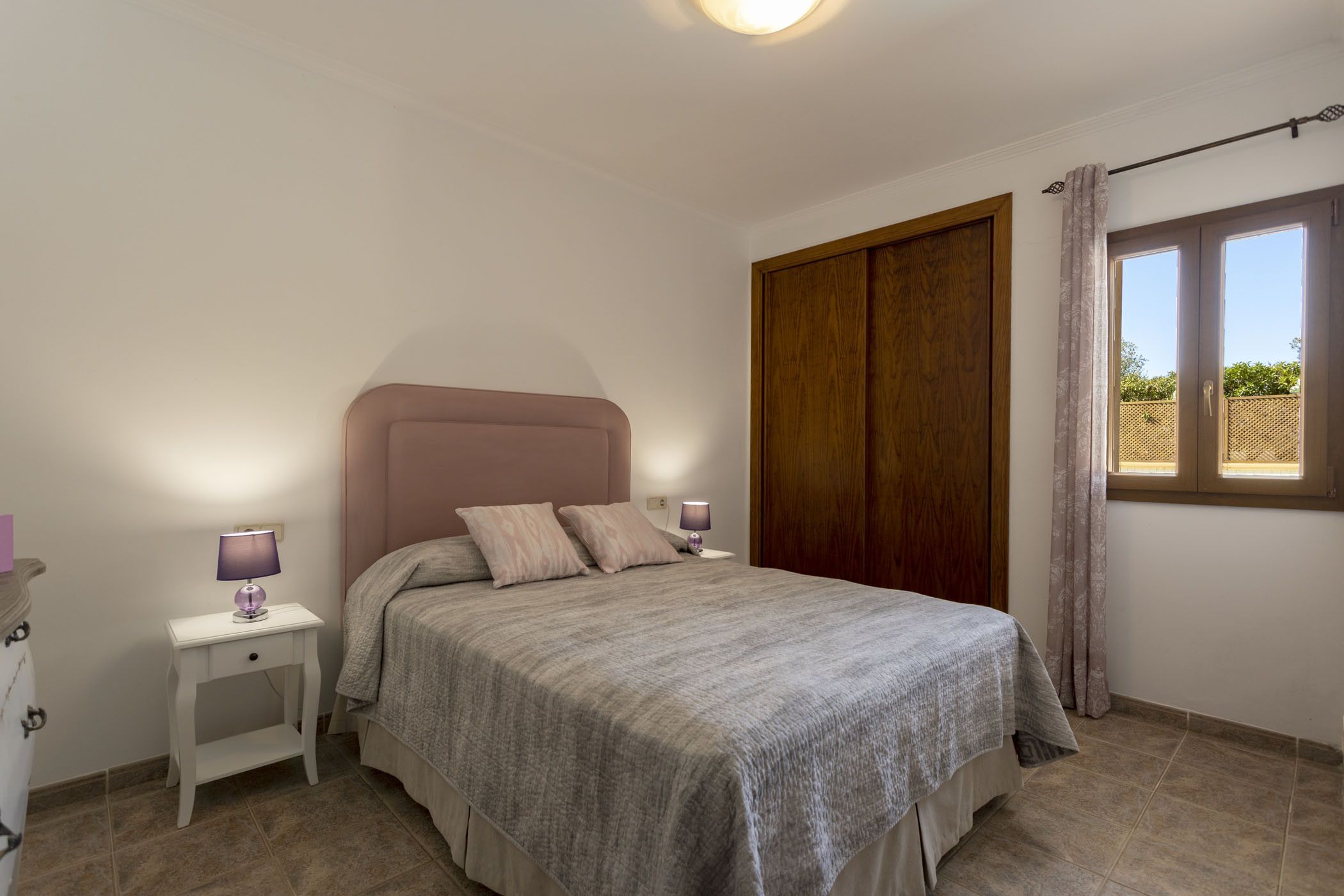 A bedroom with a bed, nightstands, a wooden wardrobe, and a window with curtains.