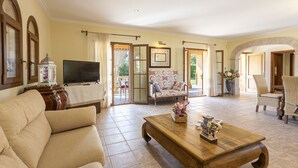 A spacious living room with a sofa, a wooden coffee table, and a television. There are two chairs and a patterned armchair. The room has a tiled floor and large windows with curtains. - Quiet villa with 4 bedrooms, 2 bathrooms, barbecue, wifi and pool (Inca)