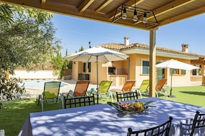 An outdoor patio with a table set for dining, surrounded by chairs and umbrellas, overlooking a swimming pool and a house with a tiled roof. - Quiet villa with 4 bedrooms, 2 bathrooms, barbecue, wifi and pool (Inca)