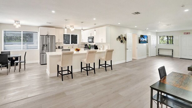 Een moderne keuken met een centraal eiland, barstoelen en een eethoek met een tafel en stoelen.