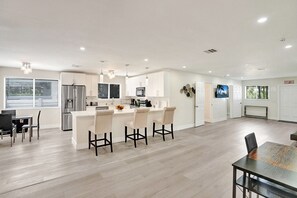 A modern kitchen with a central island, bar stools, and a dining area with a table and chairs.