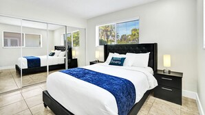 Een moderne slaapkamer met een groot bed, een spiegel en uitzicht op bomen door het raam.