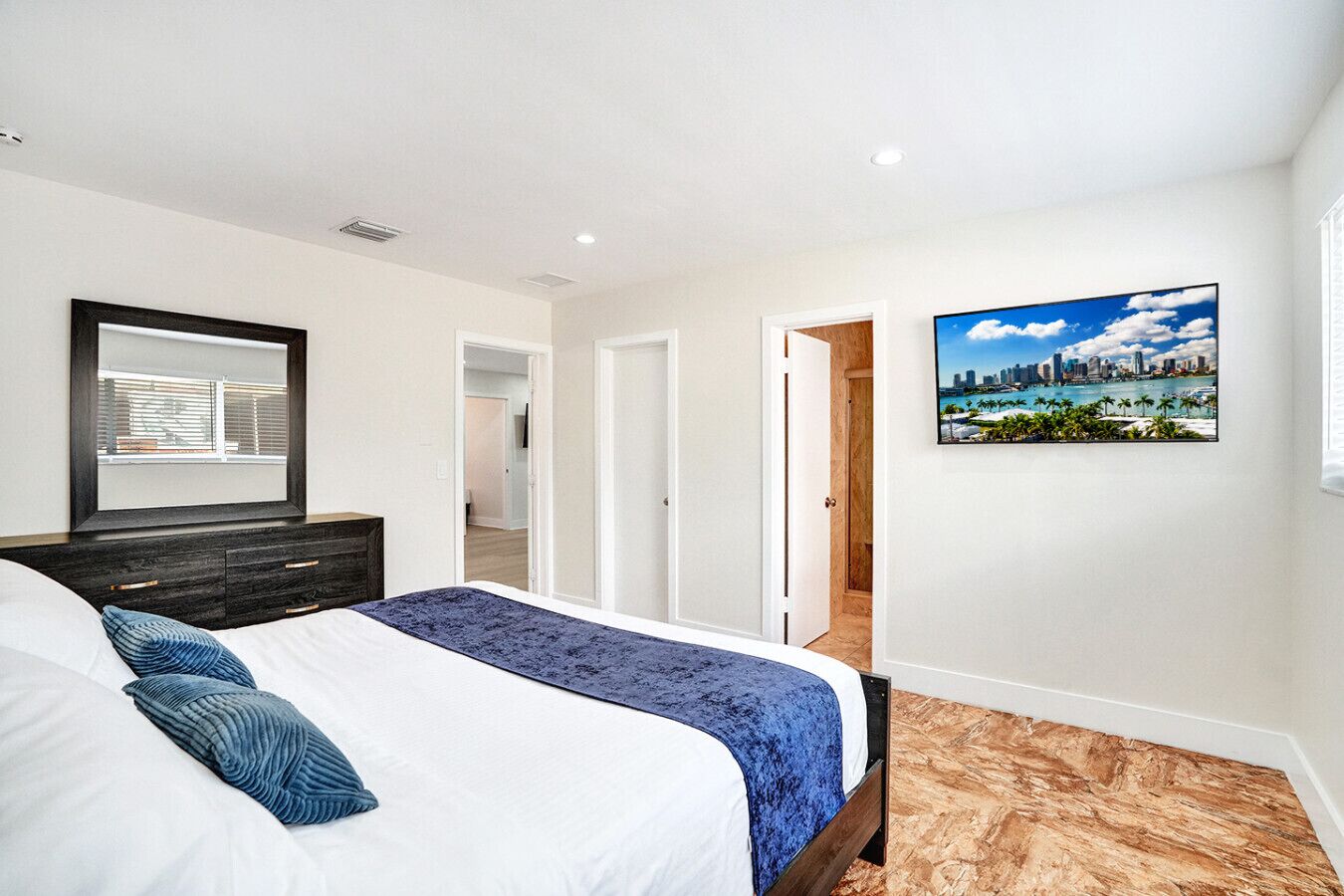 Een slaapkamer met een bed, een kaptafel, een schilderij en uitzicht op een stadsgezicht.